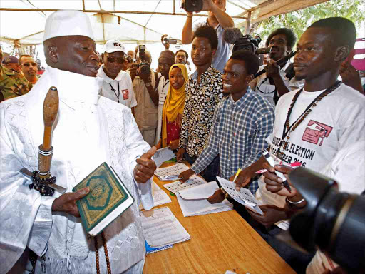 Gambian President Yahya Jammeh holds a copy of the Quran while speaking to a poll worker at a polling station during the presidential election in Banjul, Gambia, December 1, 2016. /REUTERS