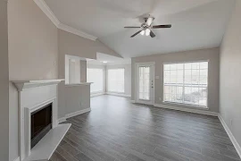 Living room with wood plank flooring, fireplace with mantel, tall ceilings, white trim and gray walls, and several windows