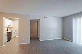 Modern, empty apartment interior with open kitchen, wood floors, and white walls.