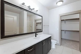 Bathroom with light walls, tile-inspired floor, a long dark vanity with stone-inspired counter with a mirror & vanity lights.