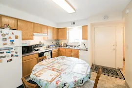 Front entry near kitchen featuring white appliances, wood cabinets, gray countertop, window above sink 