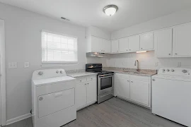 Kitchen with marbled countertops, stainless steel stove, white washer and dryer, white cabinets, and wood-inspired flooring