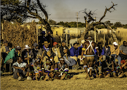 At the gifts ceremony, the initiates sit in a line on a grass mat with their fathers behind them with the elder men. At the opposite end of the field sit the mothers, mostly in their red blankets and mlinga koba (long tears). The seclusion boma can be seen behind on the left.