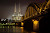 The Cologne Cathedral rises in the night sky, framed by the Opera House, Railway Bridge and Rhine River in Cologne, Germany.  The cathedral, Kölner Dom in German, is one of the most iconic landmarks in Germany.