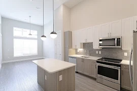 Kitchen with an island with quartz countertops facing the living area with a large window and white blinds. 