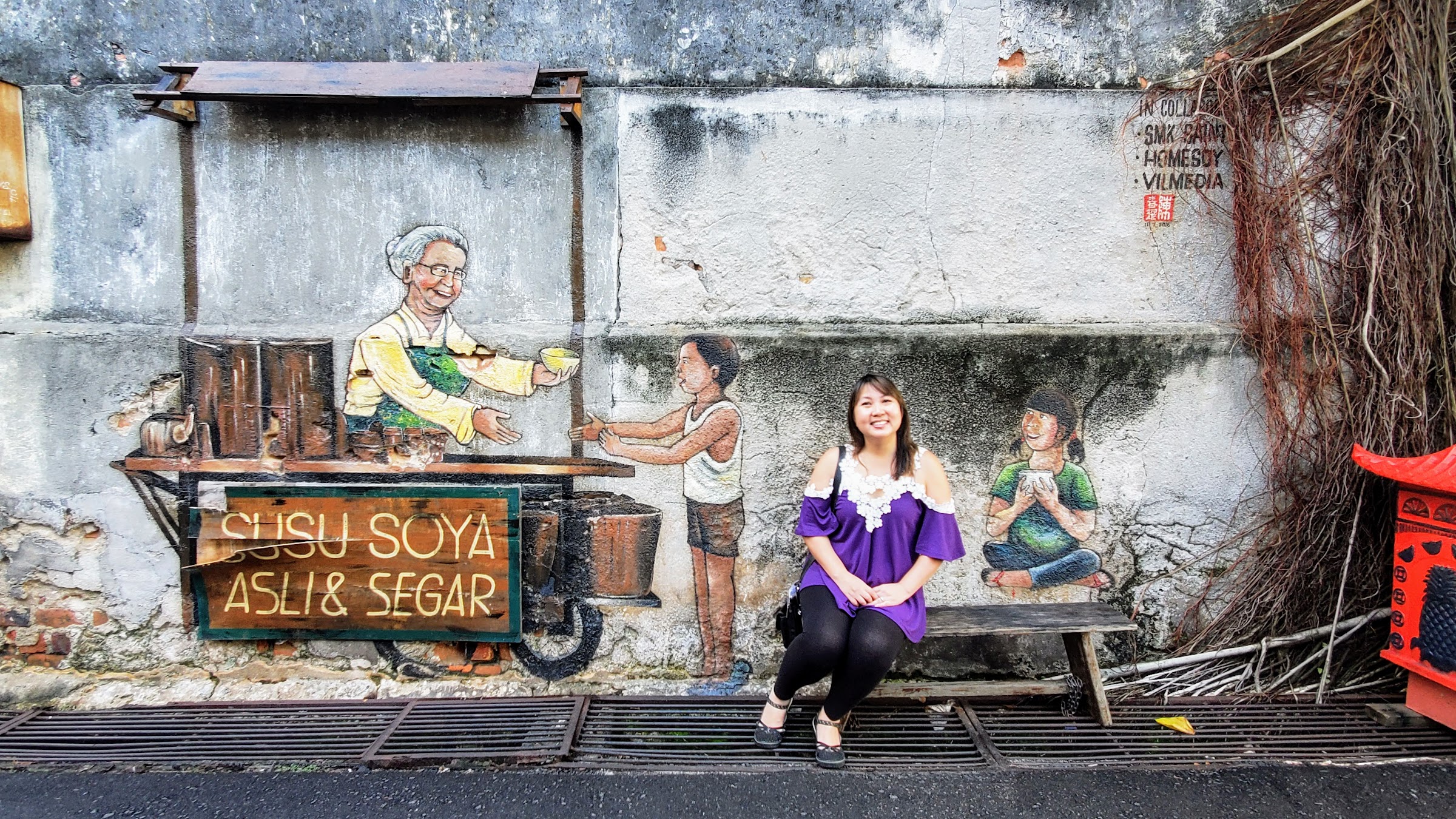 Tips on visiting George Town Street Art: Soy Milk Stall Penang mural pictures children and an old lady serving the soy bowls. Penang wall mural Old Soy Milk Stall is in a small alley off Chulia street in Penang, between Victoria Street and Armenian Street