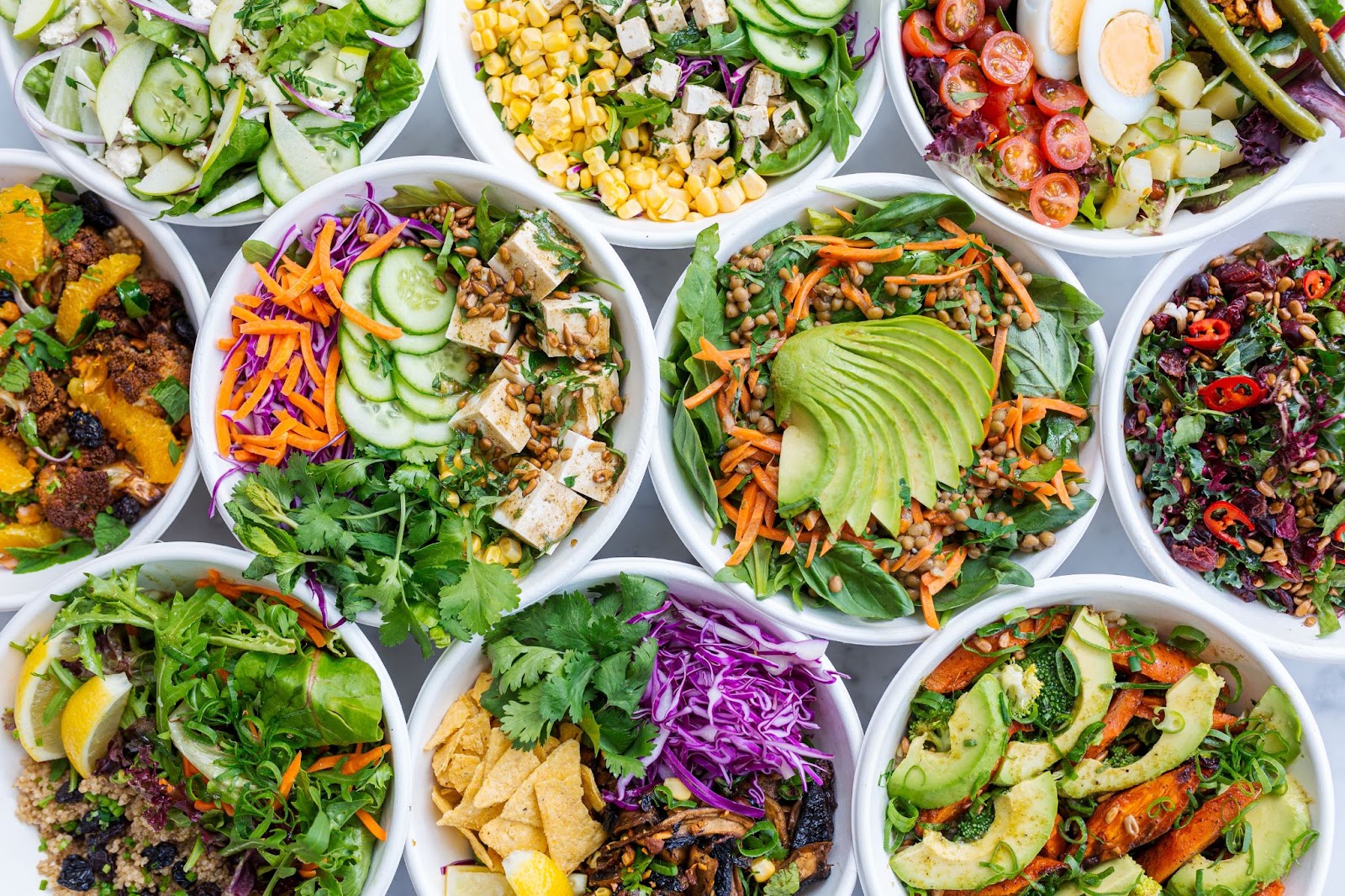 bowls of salads, viewed from the top down, with various greens, veggies, proteins and seeds