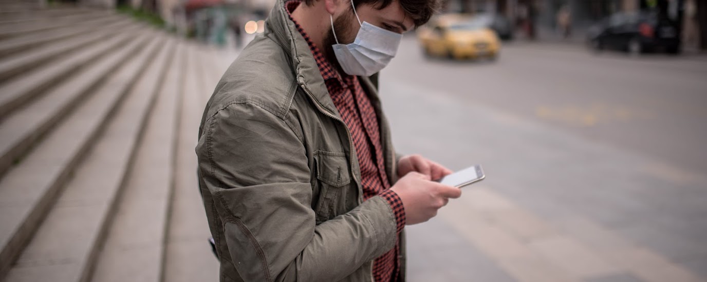 Man wearing mask on the street, shopping on his mobile device