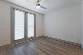 An empty apartment room with white walls, lux vinyl flooring, a ceiling fan, and a large window with closed blinds.