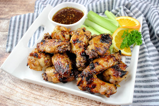A platter of Orange Glazed Chicken Wings with dipping sauce and celery.