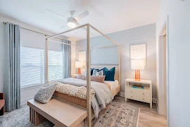 Model bedroom with framed bed, two nightstands, large windows, and wood finish flooring