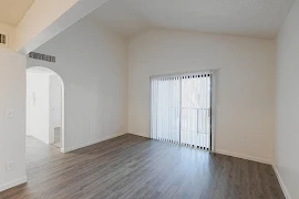 Living room with high ceilings, light walls and trim, wood-inspired flooring, double glass sliding exterior doors with blinds