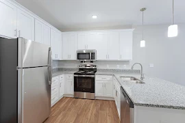 Kitchen with wood-inspired floors, neutral walls & light cabinets with stainless steel appliances and stone-inspired counter.