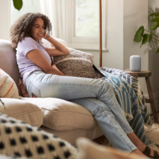 Woman sitting on living room sofa with a Nest speaker on side table.