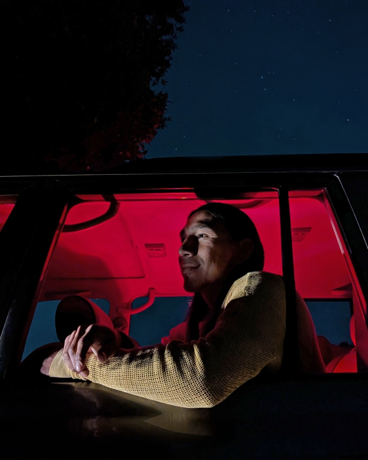 Una persona sentada en un coche durante la noche. El interior está iluminado en color rojo.