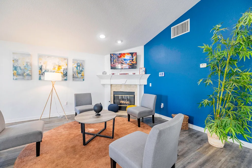 Community clubhouse with conversational seating near a fireplace with blue accent wall, wood-inspired floors & tropical plant