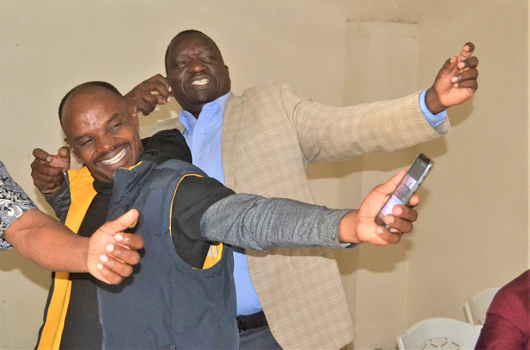 The Kitui County Boda boda chairman Kevin Kivala and the Kitui County director for Roads , transport and boda boda Benard Mulevu makes a gesture in unison during the Monday meeting.