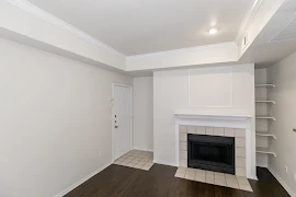 Apartment entryway leading to living area with dark wood-inspired flooring, a fireplace, and a built in shelved with lighting overhead