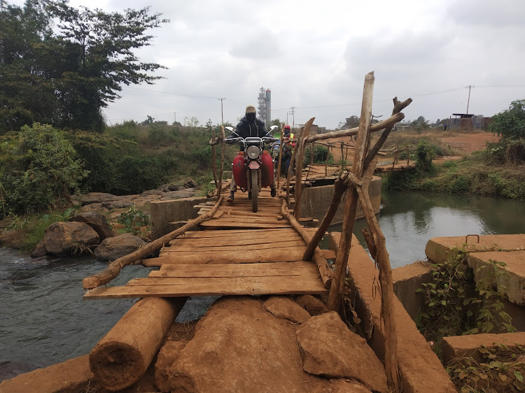 A boda boda rider crosses Mukuyu River using a makeshift bridge.