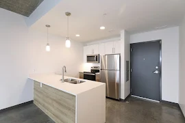 Front entry and Kitchen with peninsula and waterfall countertop, stainless steel appliances, wood lower cabinets, white upper