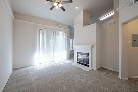 Living area with vaulted ceilings, a ceiling fan, fireplace, patio doors with vertical blinds, and carpeted flooring