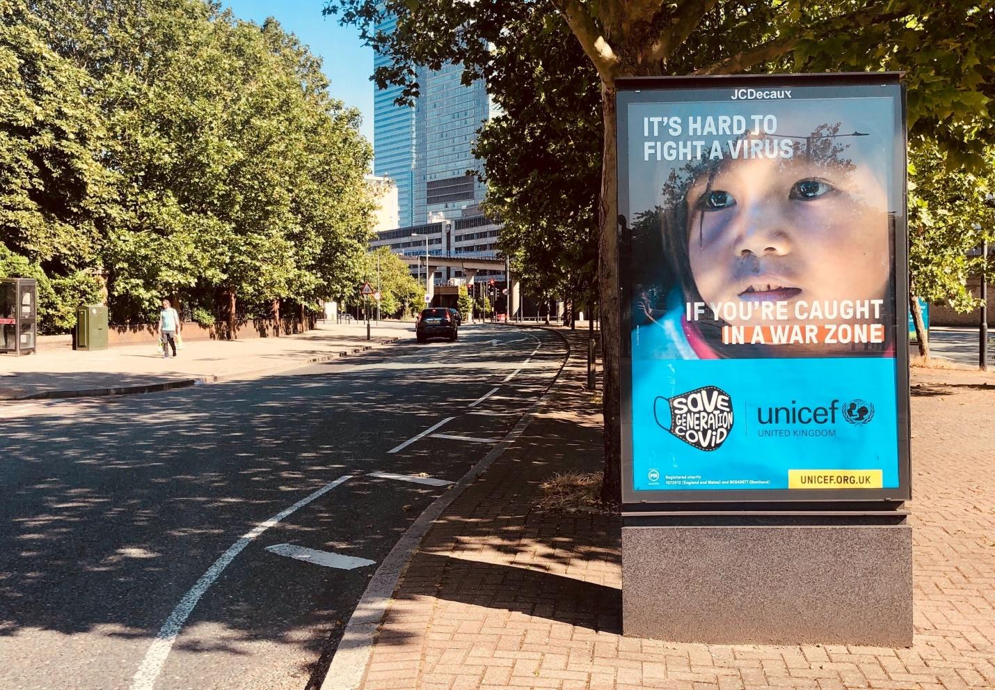 A Unicef COVID related billboard advertisement on a sidewalk.