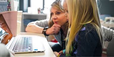 Uma professora e uma menina estão em frente a um Chromebook possivelmente lendo sobre como o Google protege as informações dos alunos e professores.