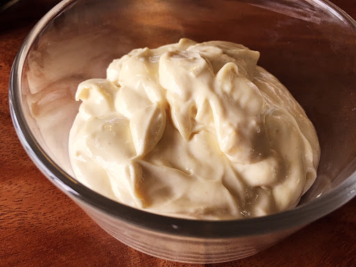 Mayonnaise in a small glass bowl sitting on a wood surface.