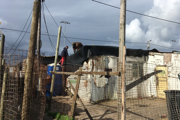 Residents repair a hole in the roof of Vuyokazi Titi’s shack in Overcome Heights in Vrygrond.