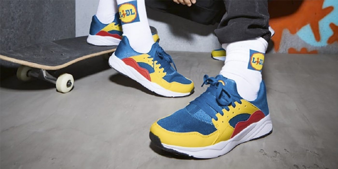 Imagen de  los pies de dos modelos vistiendo las zapatillas Lidl, en colores corporativos: azul, amarillo y rojo.