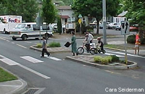 People walking and biking along a crosswalk with a refuge island on a two-lane road.