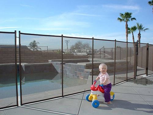 Toddler on a tricycle in front of a swimming pool mesh safety fence