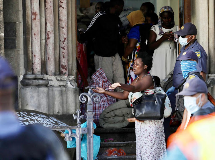 A mother with her child strapped to her back is led out of the Methodist church in Cape Town after police stormed the building on April 2 2020.