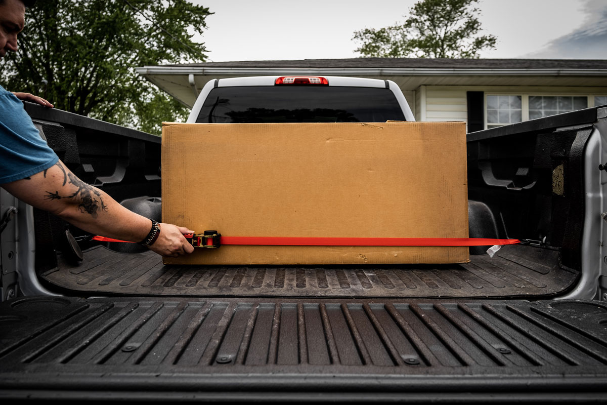 tattooed man securing box cargo on pickup truck using strapinno retractable ratchet straps