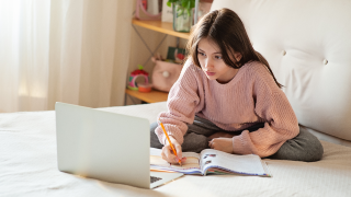 young girl sitting on bed looking at laptop