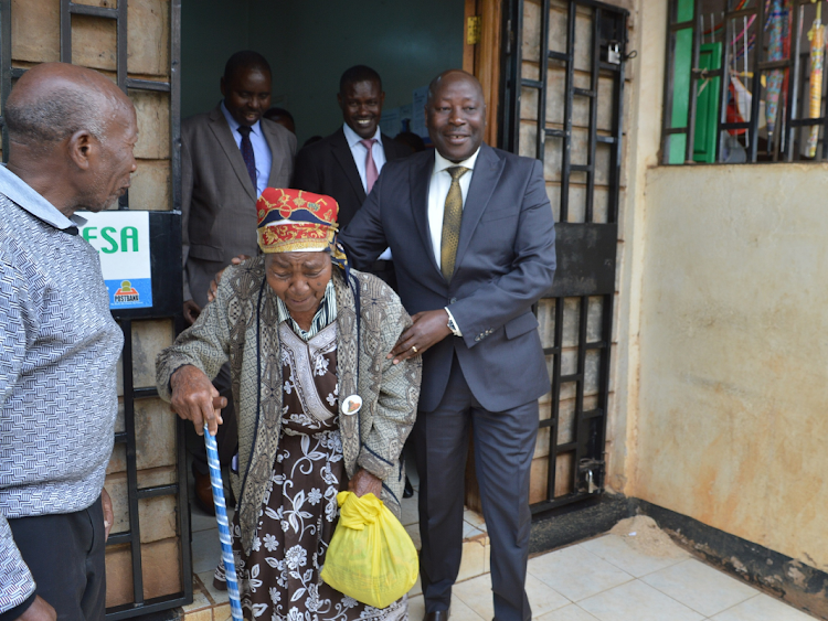 A file photo of Social Protection and Senior Citizens Affairs PS Joseph Motari assisting an elderly person who had gone to Posta Bank in Kiambu town to collect her monthly stipend.