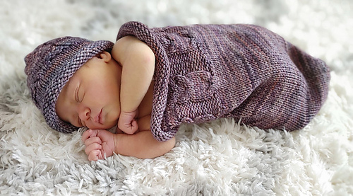 baby in a purple sleep sack with knitted owls and matching hat