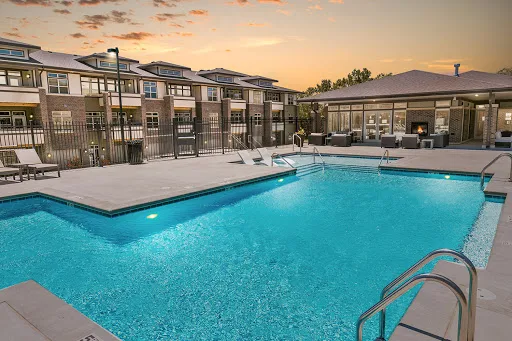 Swimming pool at dusk, next to clubhouse with an outdoor lounge area and fireplace