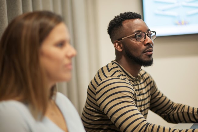 Person in white shirt sitting next to person in striped shirt with glasses