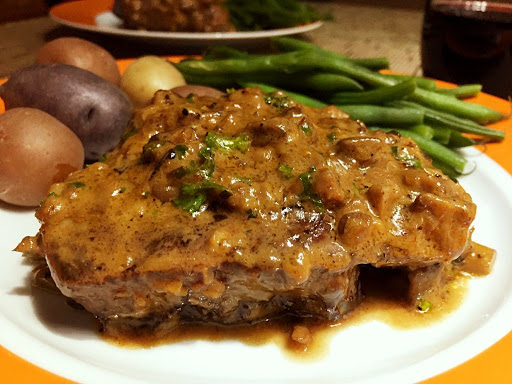 A steak topped with a brown sauce on a plate along with green beans and small potatoes.