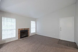 Living room with light walls, neutral carpet and a fireplace between two windows with warm toned brick surround