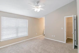 Bedroom with vaulted ceiling, ceiling fan, large window, tan walls, tan carpet, and a closet