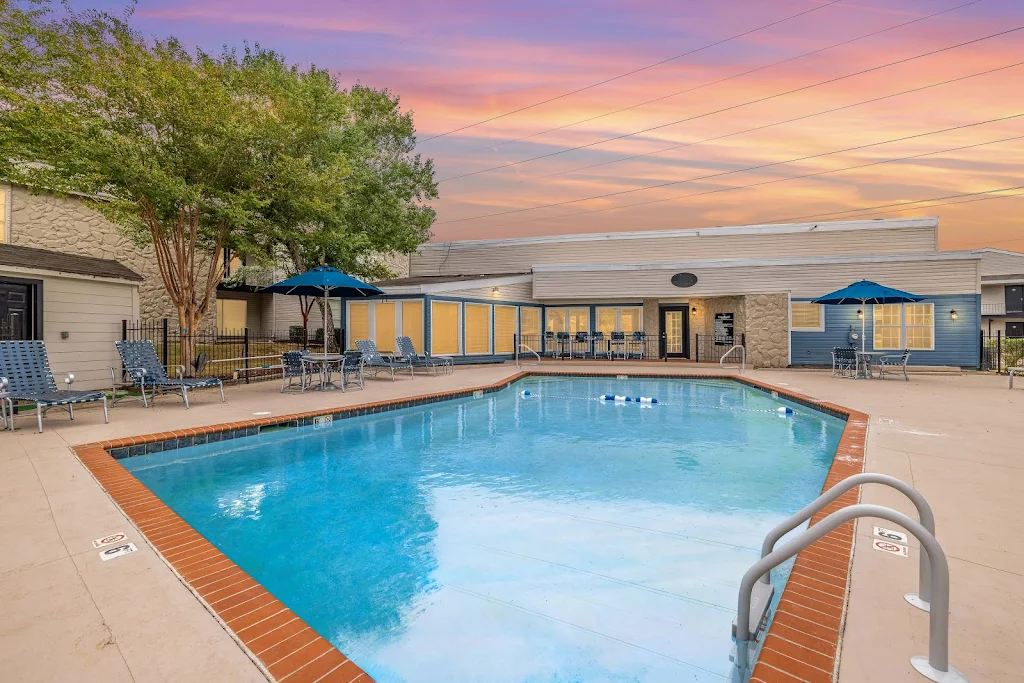 Community pool at dusk surrounded by tables and chairs. Pool is at the back of the leasing office