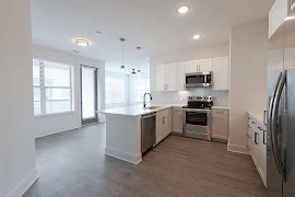 Kitchen with stainless steel appliances, white cabinets, and large windows, featuring an open layout to the living area.
