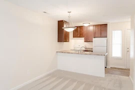 View of the kitchen from the living room with wood-inspired flooring, white appliances, and wood cabinets