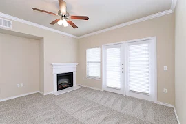 Living room with plush carpet, ceiling fan, two large doors with windows, and a fireplace