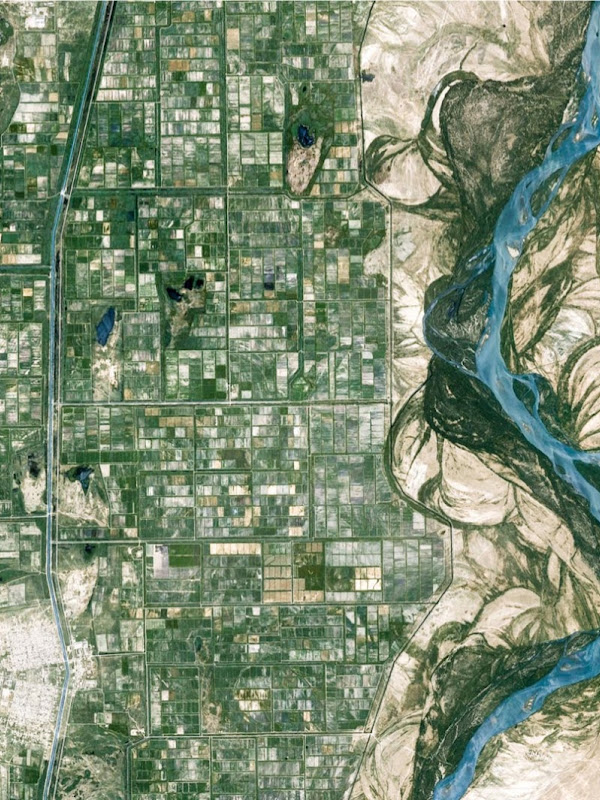 A high aerial shot of a river demarcating a city on the left and a desert on the right.