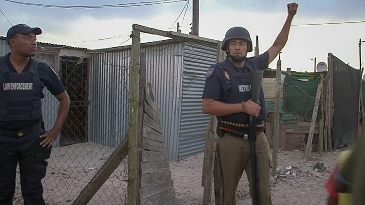 A Metro Police officer signals to other members of the Neighbourhood Safety Team during a raid in Blikkiesdorp.