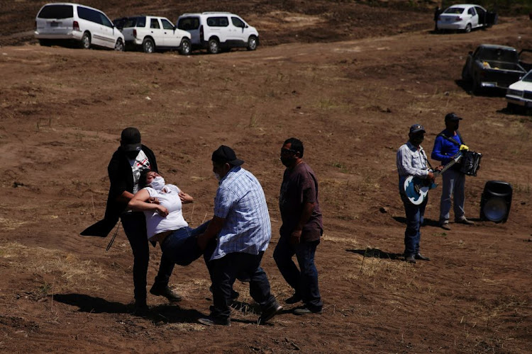 A woman overcome with emotion is carried away from a funeral at Tijuana Municipal Cemetery No. 13, where victims of the coronavirus disease are being buried, in Tijuana, Mexico, on May 7 2020.