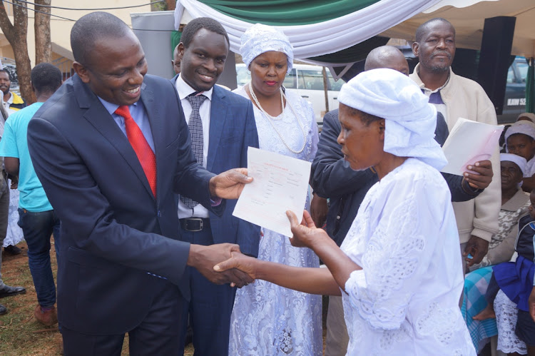 Kikuyu MP Kimani Ichung'wa hands over a birth certificate to a Shona member while Kinoo MCA Samuel Kimani looks on on Thursday, August 1